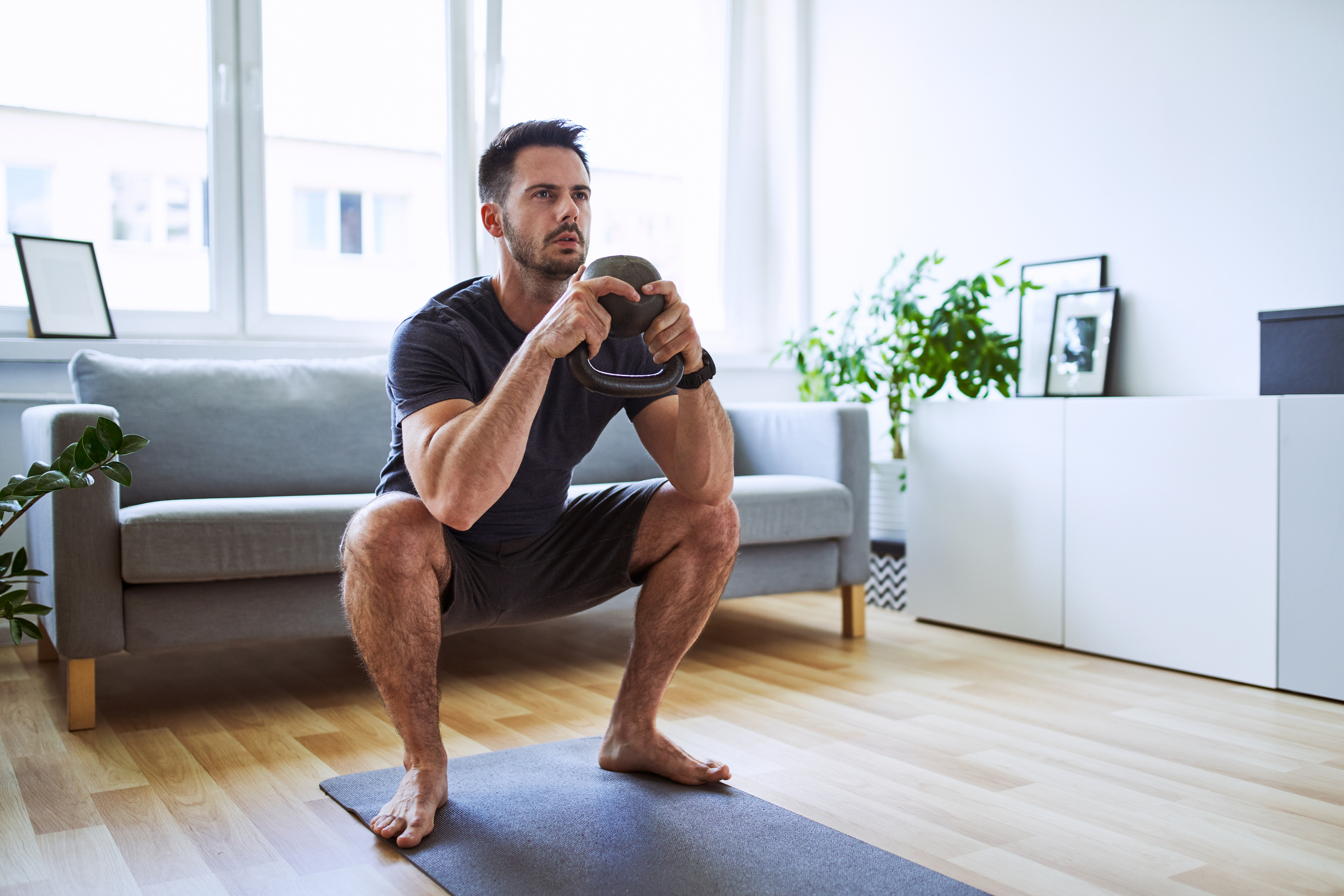 Man exercising at home doing kettlebell squat in living room